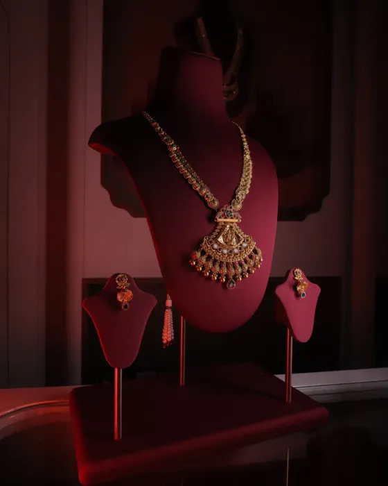 Long temple necklace with a Lakshmi pendant edged in pearls and red drops, with matching earrings, on a red velvet bust