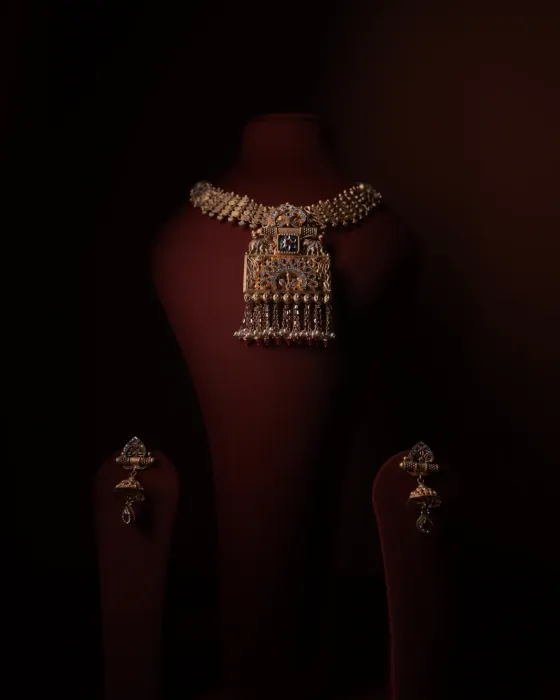 Antique gold choker with a square peacock pendant and bead tassels, with matching drop earrings, on a maroon velvet bust