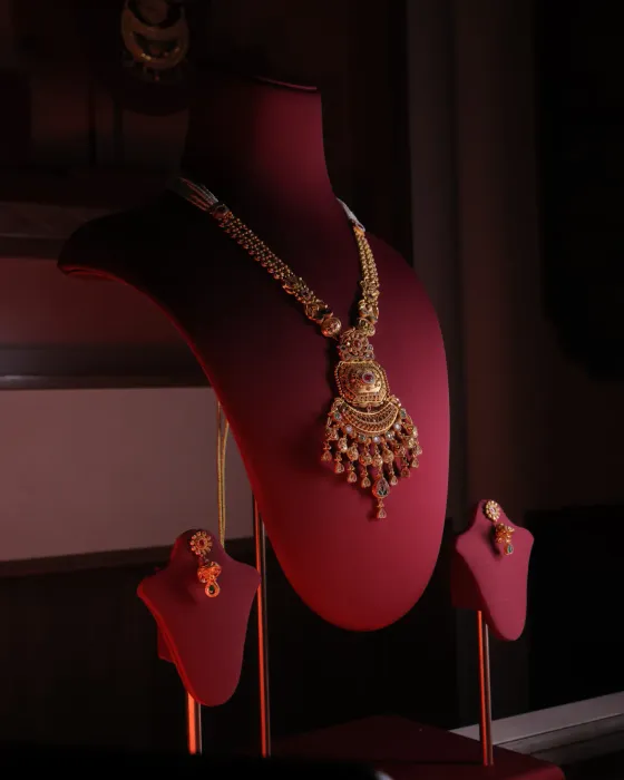 Long gold rani haar with a kundan pendant and ruby-red drops, with matching earrings, on a red velvet bust
